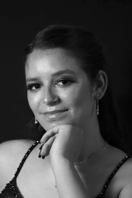 Black and white close-up portrait of a young woman with her hand resting under her chin, wearing drop earrings and a sequined top