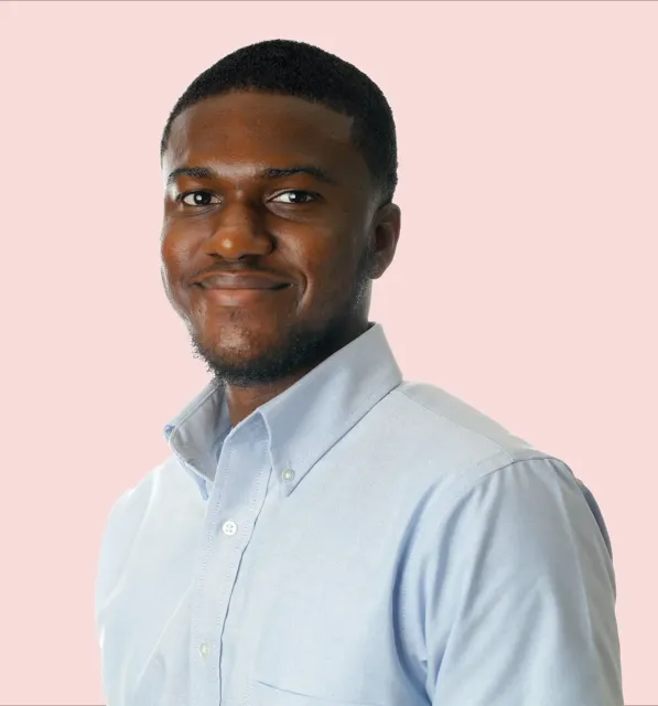 Professional headshot of a young man in a light blue button-down shirt smiling against a soft pink background