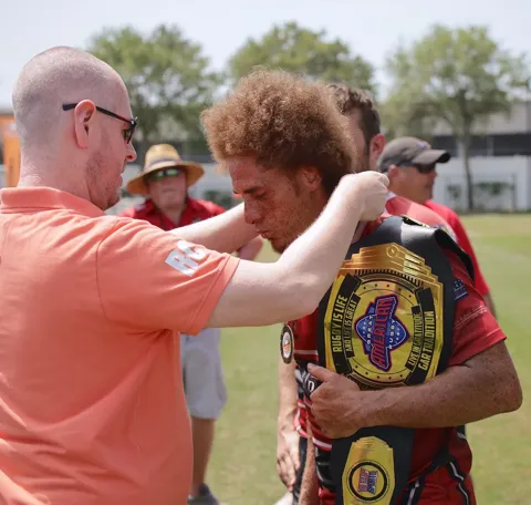 Rugby player receives the Great American Rugby championship belt award from an official during a post-match ceremony