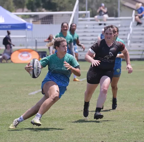 Women's rugby player in a teal jersey cuts sharply with the ball while evading a defender during a competitive match